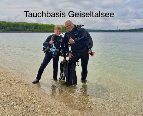 Zwei Männer in Tauchanzügen geben Daumen hoch am Ufer des Geiselhaltsees.
